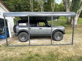 Veikous metal carport covering a parked SUV in the grass